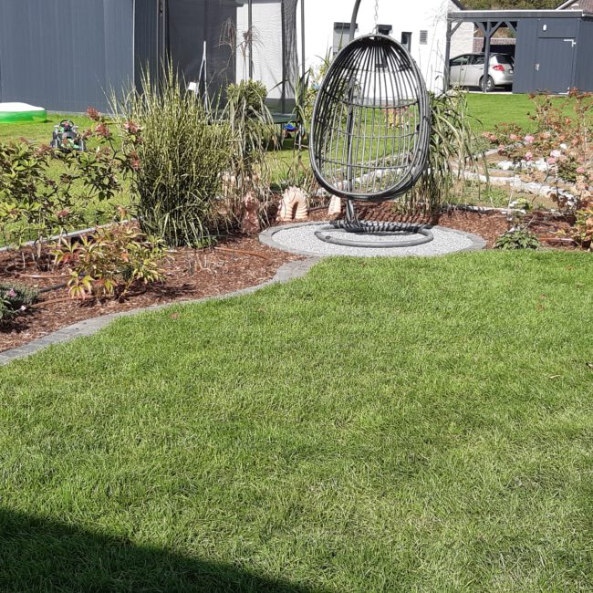 Gemütlicher kleiner Rasen umgeben von Beeten mit einem Hängesitz in der Ecke