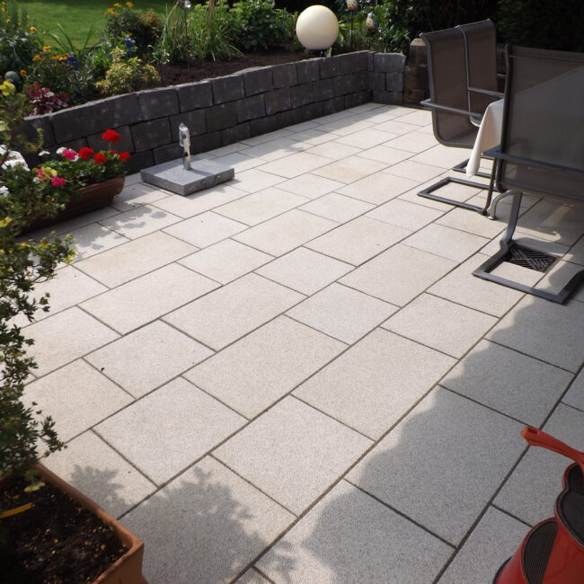 Steinterrasse aus klassischen Platten umgeben von einer kleinen Mauer mit Rosenbeeten