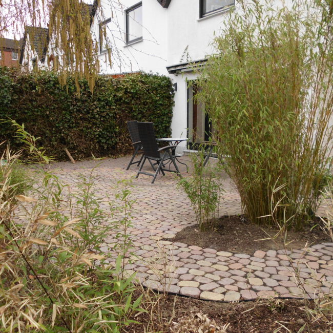 Terrasse aus Kopfsteinpflaster, die ein zentrales Bambusbeet umrandet