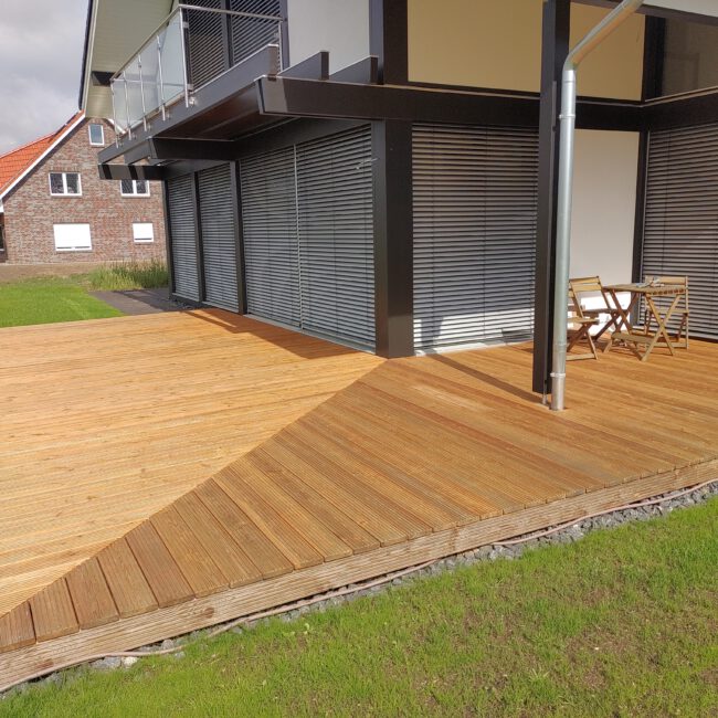 Holzterrasse auf einer Rasenfläche um die Ecke eines Hauses gebaut