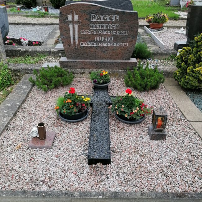 Foto eines Grabes mit Kiesboden, Kerzen und einem Steinkreuz als Zentrum